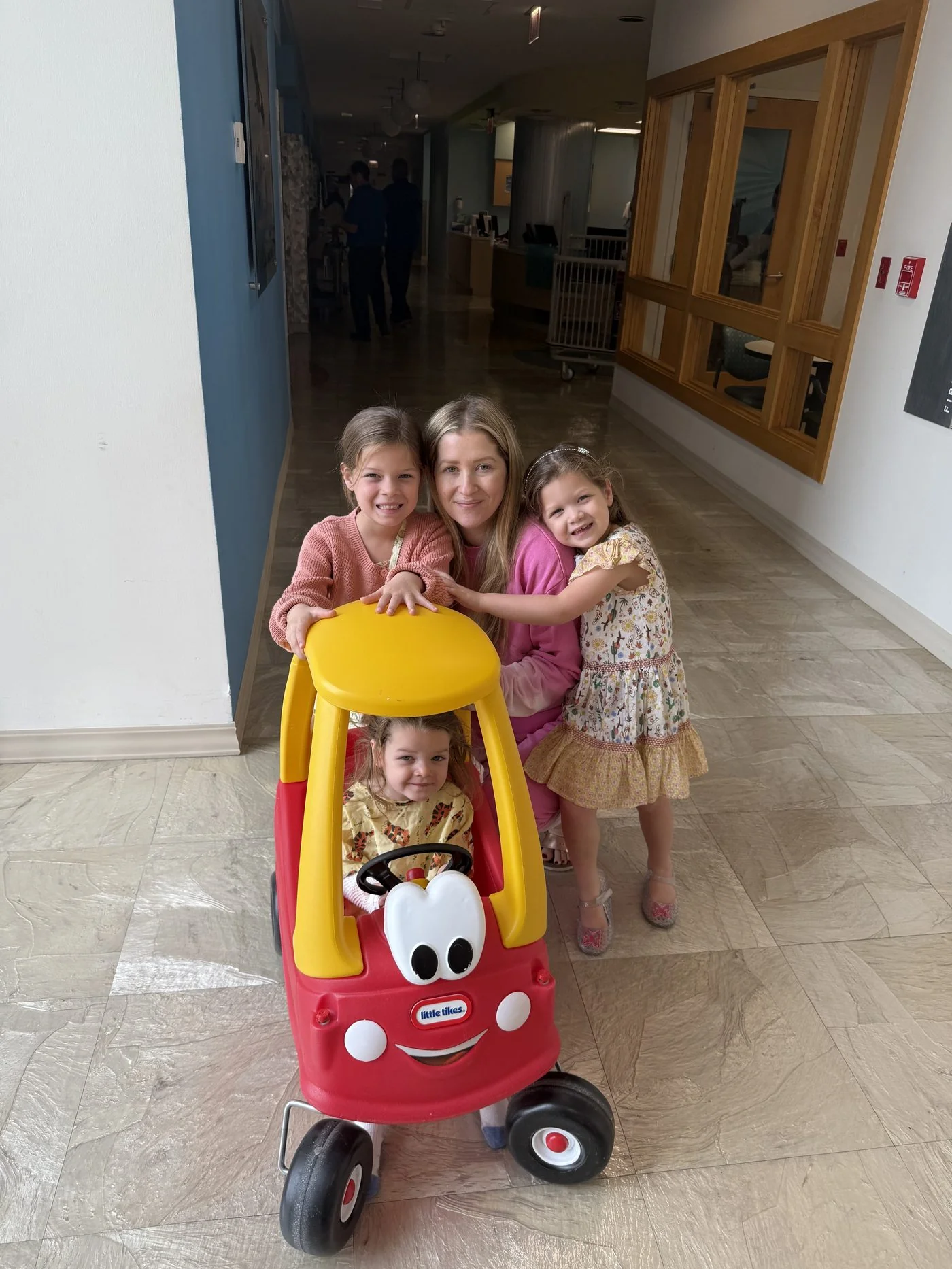 Isa in a toy car with her mother Rachel and her sisters at the hospital