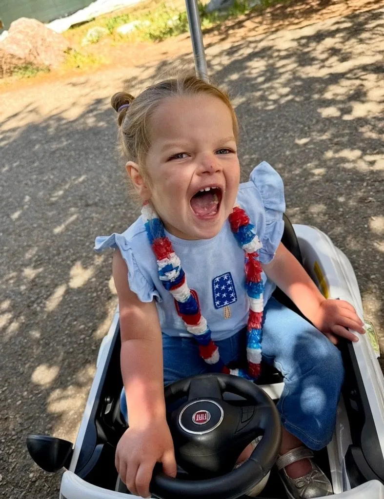 Isa laughing in a toy car outdoors